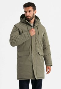 Olivgrüner, gepolsterter Parka mit Kapuze, Frontreißverschluss, zwei großen aufgesetzten Taschen und Rippbündchen. Das Material wirkt glatt und strapazierfähig.