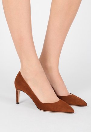 Beneden met bruine suède pumps met een puntige neus en slanke middelhoog stilettohak op een witte achtergrond.
