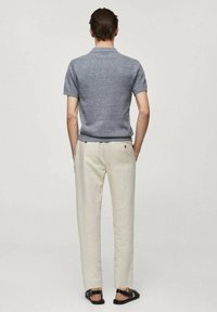 Tenue décontractée pour homme comprenant un polo gris à manches courtes, un pantalon beige et des sandales noires, mettant en avant des lignes simples et épurées ainsi que des textures douces.