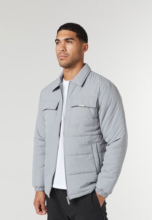 Chaqueta acolchada gris con cremallera delantera, dos bolsillos en el pecho y puños elásticos. Material ligero con una textura suave.