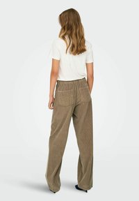 Brūni korduroja platajām biksēm ar elastīgu jostu, ar divām aizmugurējām kabatām. Apvienotas ar vienkāršu baltu T-kreklu.