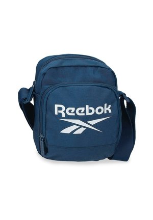 Bolso bandolera compacto azul marino con correa ajustable, bolsillo delantero con cremallera y logotipo blanco de Reebok en el panel frontal.