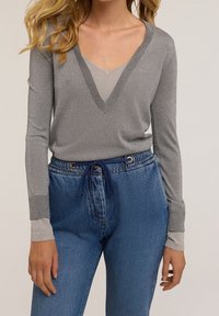 Haut gris à manches longues avec un col en V et un col contrastant ; associé à un jean en denim bleu taille haute avec une taille à cordon et une coupe décontractée.