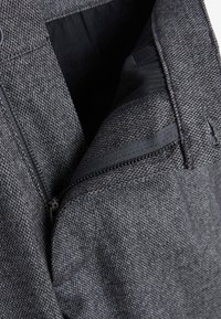 Tela texturizada gris con un bolsillo con cremallera y un forro interior suave visible. El diseño presenta un corte moderno y un detalle de patrón sutil.
