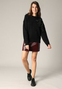 Pull noir, texturé, avec une coupe ample et un détail brodé en forme de feuille sur une épaule, associé à une mini-jupe bordeaux brillante. Chaussures noires à lacets.