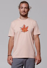 Lichtroze t-shirt met korte mouwen en een geometrisch oranje esdoornbladlogo op de borst, gemaakt van zachte katoen.