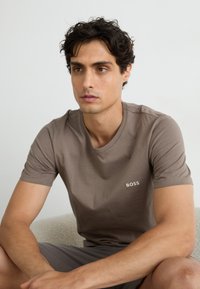 T-shirt en coton marron avec un col rond et des manches courtes. Présente un petit logo brodé "BOSS" de couleur claire sur la poitrine.