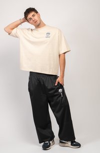 Beige oversized cotton t-shirt with blue graphic print on chest, paired with black satin track pants featuring white side stripes and logo.
