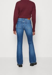 Uppklippta blå denimjeans med medelton, med bakfickor och en brun läderlogotyp vid midjan.