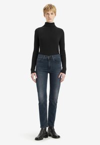 Zwart ribbel turtleneck trui, slim fit. Donkerblauwe denim jeans, rechte pijp, lichte slijtage. Zwarte enkellaarsjes met stevige hakken.