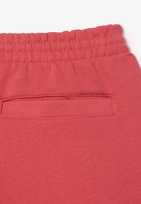 Los joggers de algodón color coral cuentan con una cinturilla elástica y un pequeño bolsillo trasero, mostrando una textura suave y un diseño minimalista.