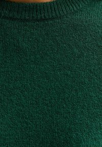Ciemnozielona dzianina swetra z okrągłym dekoltem i prążkowanym wykończeniem. Tekstura wydaje się miękka, z jednolitym, nieco puszystym wykończeniem.