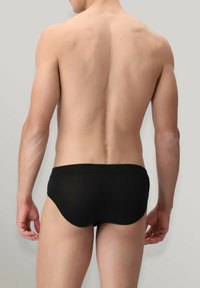 Costumi da bagno neri in microfibra liscia, design a vita bassa e comoda cintura elastica. Sullo sfondo c'è un grigio neutro.