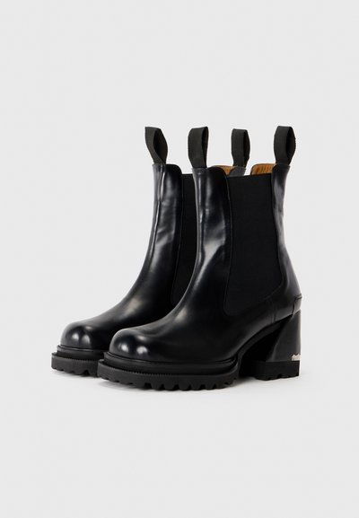 Bottines Chelsea en cuir noir avec des talons épais, des panneaux latéraux élastiques, des semelles robustes et des anses en tissu sur le dessus.