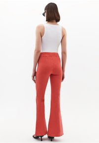 Rode flared broeken van denim, met een hoge taille, gladde textuur, gecombineerd met een witte tanktop. Effen achtergrond voor contrast.
