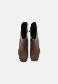 Pár hnědých kožených kotníkových bot se čtveratými špičkami a bočními zipy, pohled shora na světlém pozadí.