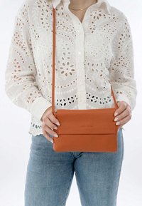 Orange Leder Crossbody-Tasche mit einer glatten Textur und minimalistischen Design. Die Tasche verfügt über einen Klappdeckel und einen verstellbaren Riemen.