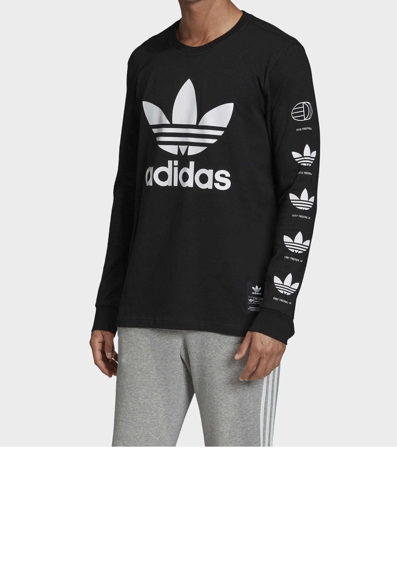 Black long-sleeve t-shirt with white Adidas logo and three stripes design on the front; features repeated logo accents on sleeves.