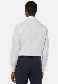 Weißes Langarmhemd mit tailliertem Schnitt und klassischem Kragen, kombiniert mit dunkelblauen Hosen und einem schwarzen Gürtel. Glattes Material, formelles Design.