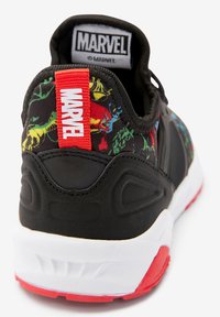 Svart atletisk sko med färgglada superhjältegrafik, röd detalj på hälfliken och en vit mellansula med röd yttersula.