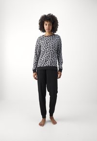 Tigerskinnstryka i grå nyanser med svarta accenter, i kombination med svarta snäva byxor. Outfiten har en mjuk textur och elastiska manschetter.