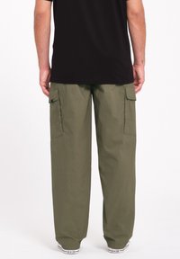 Pantalons cargo en vert olive, avec des poches latérales, une coupe décontractée et des poignets fuselés. Portés avec un T-shirt noir et des baskets blanches.