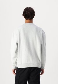 Felpa grigia a girocollo realizzata in morbido cotone. Presenta maniche lunghe e polsini a costine, con una vestibilità rilassata e un design semplice.