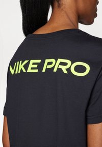 Sort Nike Pro t-shirt med limegrønt tekst på ryggen. Har en rund halsudskæring og korte ærmer, fremhæver et glat, let stof.