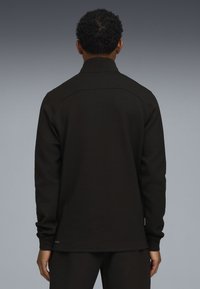 Camisa negra de manga larga con cuello alto, diseñada con una textura suave y detalles de costura mínimos en los hombros y el dobladillo.