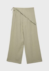 Pantalon beige à jambes larges avec taille haute ceinturée, fermeture à nouer, et petits clous métalliques le long de la ceinture diagonale.