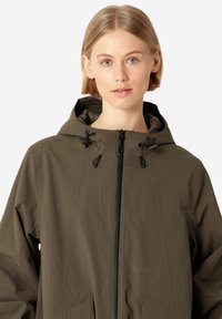 Chaqueta verde oliva con capucha, que presenta un cierre con cremallera y dos bolsillos en la parte frontal. La tela tiene una sutil textura vertical.