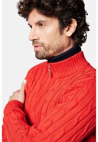 Czerwony sweter z dzianiny z wysokim kołnierzem i zamkiem, wyróżniający się wzorem w warkocze. Długie rękawy z ściągaczami i dopasowany krój.