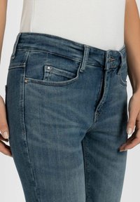 Jeans de mezclilla azul oscuro con una cintura alta, cinco bolsillos y detalles de costura sutiles. La tela tiene una textura suave con un ligero desgaste.