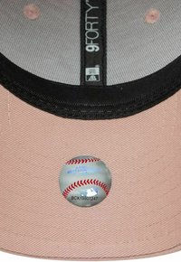 Cappello di stoffa rosa con visiera nera, superficie texturizzata e adesivo di baseball argentato con cuciture rosse sulla fascia interna.