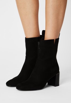 Stivali alla caviglia in suede nero con punta affilata, zip laterale e tacco a blocco. Presentano inoltre dettagli intagliati nella parte superiore per un design aggiuntivo.