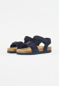 Marinblå sandaler med två justerbara remmar, korkfotbädd och texturerad gummisula. Har en slät yta och en spänndetalj.