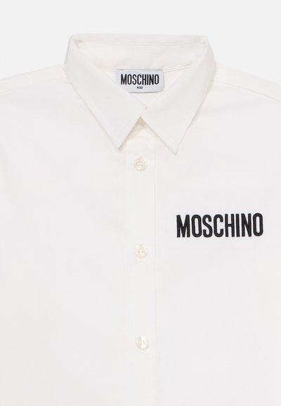 Hvit langermet skjorte med knapp og spiss krave, samt svart "MOSCHINO"-logo brodert på brystet.