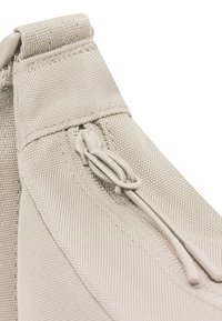Primer plano de tela beige con una cremallera visible y una lengüeta, mostrando costuras detalladas y textura.