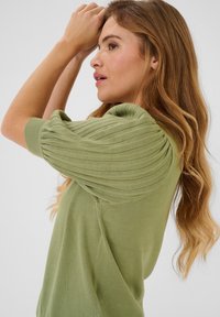 Top verde in maglia con pieghe arricciate sulle maniche corte, texture morbida e vestibilità rilassata, che mette in mostra uno stile casual.