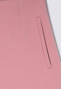 Primo piano di un tessuto rosa di un indumento che presenta una tasca con fessura. La texture è liscia, con dettagli di cucitura sottili lungo i bordi.