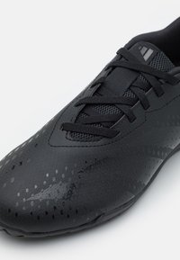 Czarne buty sportowe z teksturowanym syntetycznym cholewką, sznurowanym zapięciem, panelami z siateczki i subtelnymi wzorami. Zaokrąglony czubek i niskoprofilowa podeszwa.