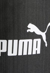 Un tissu noir à l'aspect texturé présente un grand logo "PUMA" blanc et une silhouette blanche d'un puma en train de sauter.