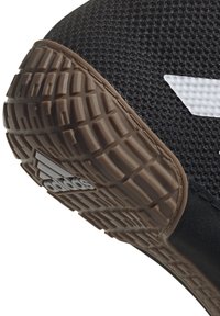 Närbild av en svart Adidas-sneaker som visar en texturerad brun sula med logotyp och en ovandel i mesh med vit rand.