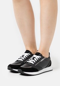 Baskets noires et grises avec une tige lisse en cuir et daim, dotées de lacets blancs, de panneaux en mesh et d'une semelle plate en caoutchouc.