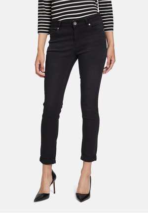 Black skinny jeans with a smooth texture, five-pocket design, and rolled cuffs, paired with pointed black heels and a striped top.