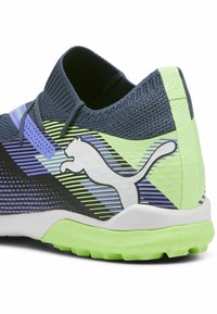 Scarpa sportiva Puma con tomaia in maglia blu scuro decorata da strisce diagonali verdi e viola e logo, suola bianca con battistrada verde texturizzato.