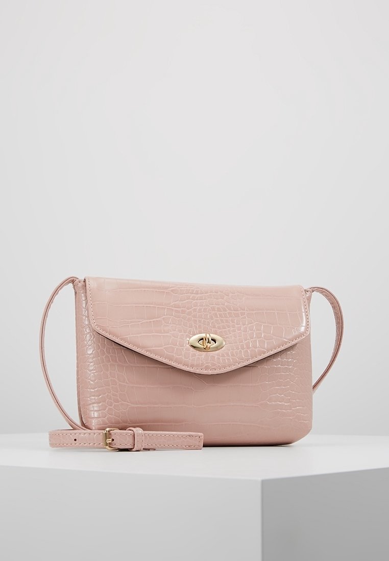 Pink crocodile-textured handbag with a flap closure, gold hardware, adjustable strap, and smooth finish. Compact and rectangular design.