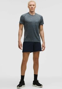 Sportowy strój składający się z teksturowanej, ciemnoszarej koszulki z krótkim rękawem oraz granatowych szortów. Model nosi czarne sneakersy z białymi podeszwami.