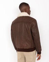 Chaqueta bomber de cuero marrón con cuello de piel crema, puños acanalados y cintura ajustada. Textura suave con una forma entallada, diseñada para proporcionar calor.