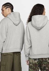 Sivi puloverji s kapuco z mehko teksturo, z rebrastimi manšetami in spodnjim robom. Eden ima olivne taktične hlače, drugi vzorčaste maskirne hlače.